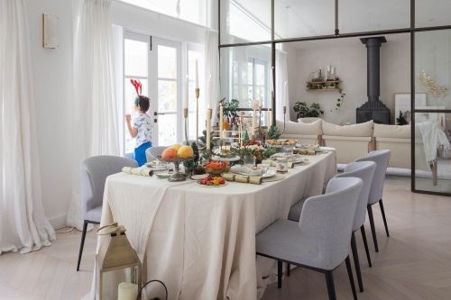 Boy looking out window with prepared Christmas meal in foreground - Australian Stock Image