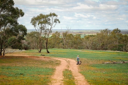 Boy riding bike on dirt track with view of fields in the distance - Australian Stock Image