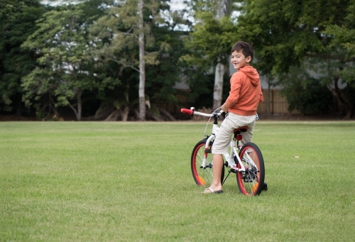 Boy riding orange bicycle on lawn. - Australian Stock Image