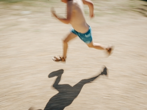 Boy running in swimmers with shadow and motion blur - Australian Stock Image