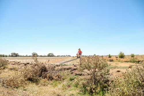 Boy sitting on farm fence in dry summer conditions - Australian Stock Image