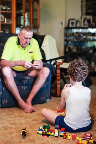 Boy sitting with grandfather playing with blocks together - Australian Stock Image