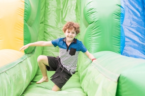 Boy smiling on knee on blow up slide at local show - Australian Stock Image