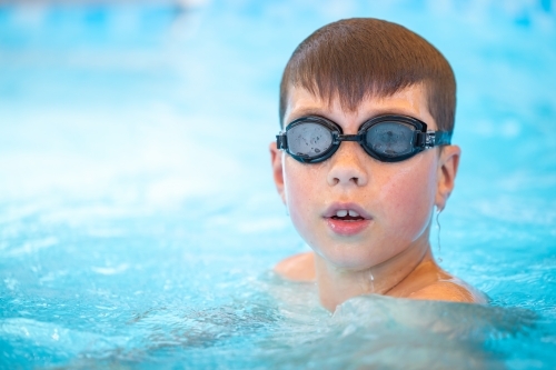 Boy swimming in pool wearing goggles - Australian Stock Image