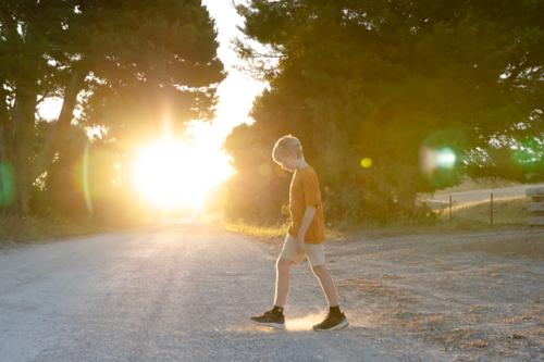 Boy walking on rural country road at sunset from farm - Australian Stock Image