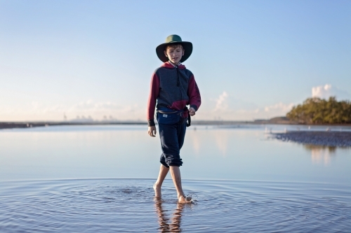 Boy walks on the beach at lowtide in winter barefoot - Australian Stock Image