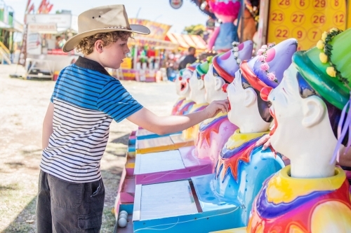 Boy wearing akubra hat placing ball in mouth of clowns sideshow alley at local show