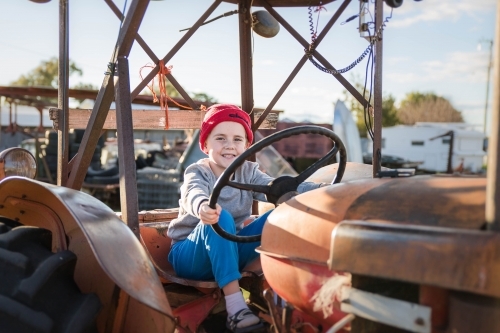 Boy wearing beanie sitting on old tractor holding steering wheel - Australian Stock Image