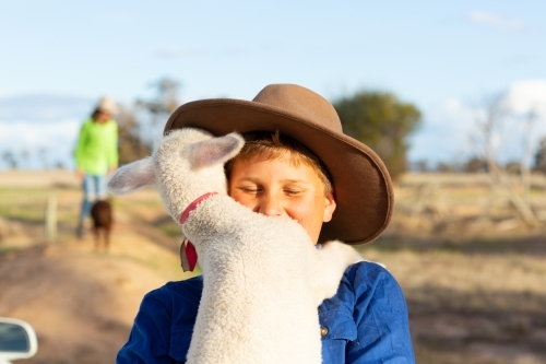 Boy wearing hat holding his pet lamb - Australian Stock Image