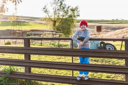 Boy with beanie standing on fence of sheep yards - Australian Stock Image