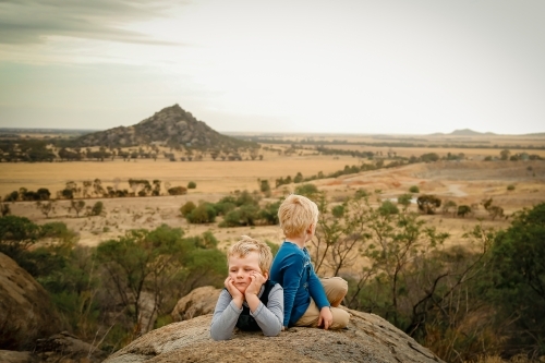 Boys relaxing on rock on outdoor adventure in Central Victoria with Pyramid Hill in background - Australian Stock Image