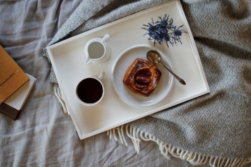 Breakfast on tray sitting on bed with books - Australian Stock Image