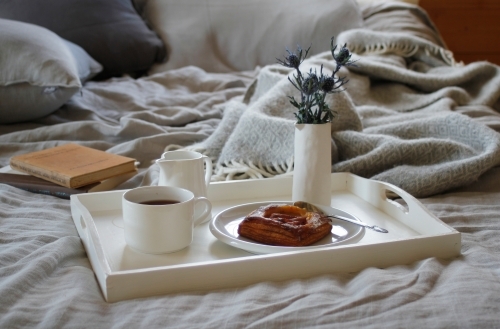 Breakfast tray on bed with grey linen and books - Australian Stock Image