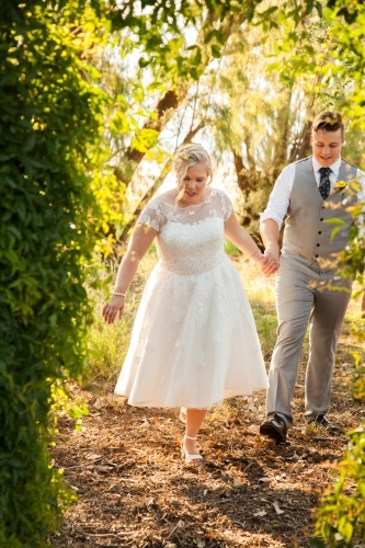 Bride walking with groom through arch in garden - Australian Stock Image