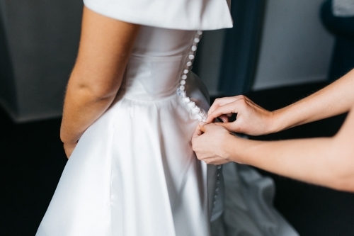 Brides wedding dress being buttoned up by bridesmaid - Australian Stock Image