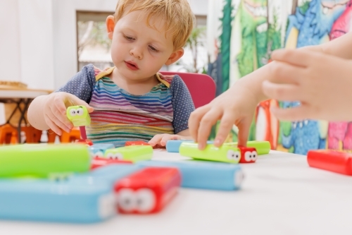 Brightly coloured building blocks on table with children in background - Australian Stock Image