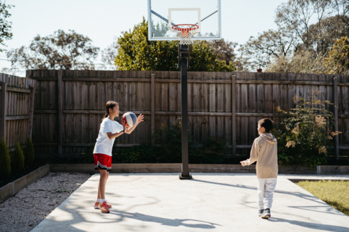 Brother and sister playing basketball in their back yard - Australian Stock Image