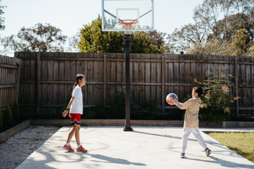 Brother and sister playing basketball in their backyard - Australian Stock Image