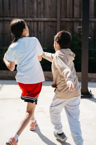 Brother and sister playing basketball in their yard at home - Australian Stock Image