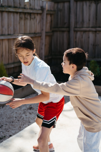 Brother and sister playing basketball in their yard. - Australian Stock Image