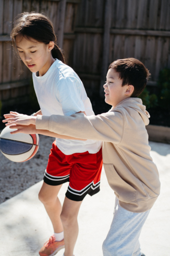 Brother and sister playing basketball in their yard. - Australian Stock Image