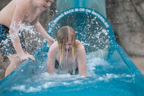 Brothers playing at the bottom of a waterslide on holiday - Australian Stock Image
