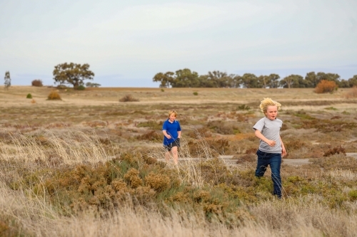 Brothers running while exploring desolate dry lake together. Family outing in the Australian bush. - Australian Stock Image
