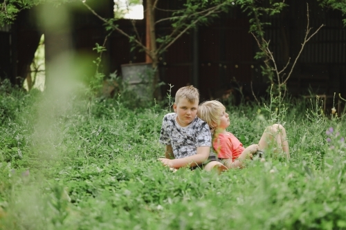 Brothers sitting together in long grass on farm - Australian Stock Image