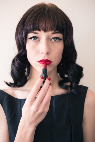 Brunette woman holding red lipstick to her lips staring into camera - Australian Stock Image