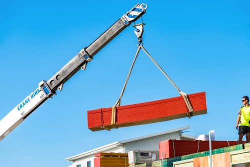 Building material being lifted by a crane to the second level with man observing - Australian Stock Image