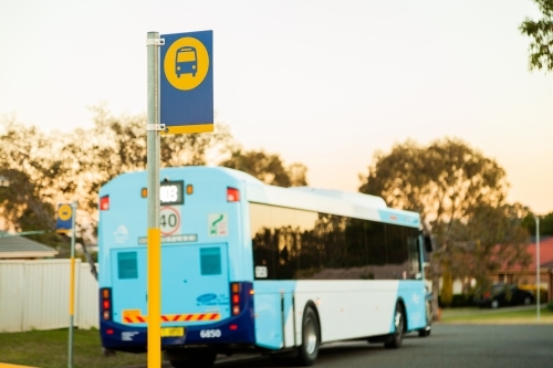 Bus travelling down road past bus stop sign - Australian Stock Image