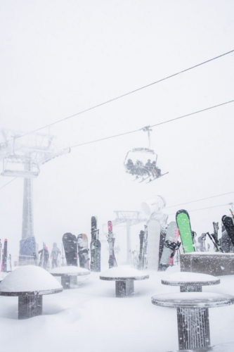 Cafe tables covered in snow with skiers on ski lift above - Australian Stock Image