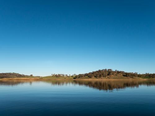 Calm rural water storage dam with a large reflected blue sky - Australian Stock Image