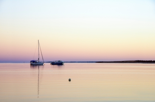 Calm Waters for a fishing boat in the early morning hours against a pastel skyline. - Australian Stock Image