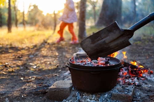 Camp oven over campfire cooking dinner - kids play nearby fire - Australian Stock Image