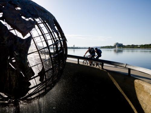 Captain Cook Memorial Globe with two cyclists and Lake Burley Griffin - Australian Stock Image