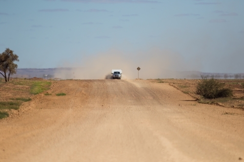 Car and caravan being driven along a wide outback road