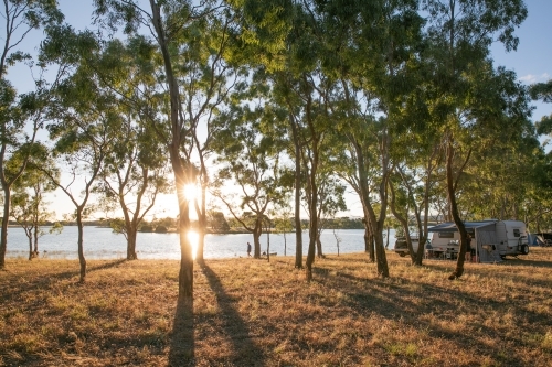 Caravan by a lake with long shadows in the late afternoon light and person walking. - Australian Stock Image