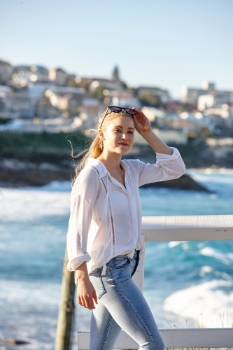 Carefree young blonde-haired woman at beach holding sunglasses