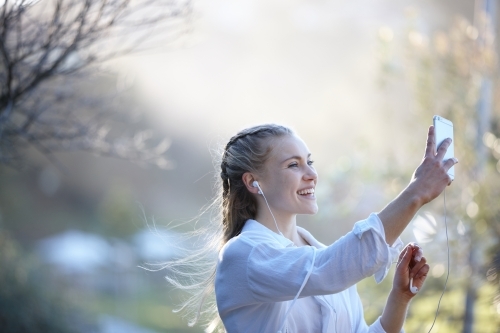 Carefree young blonde-haired woman listening to music with headphones outdoors - Australian Stock Image