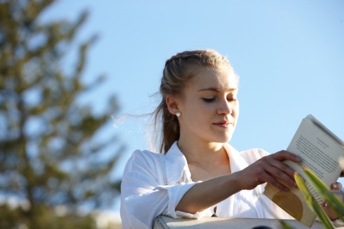 Carefree young blonde-haired woman reading book outdoors in the sunshine - Australian Stock Image