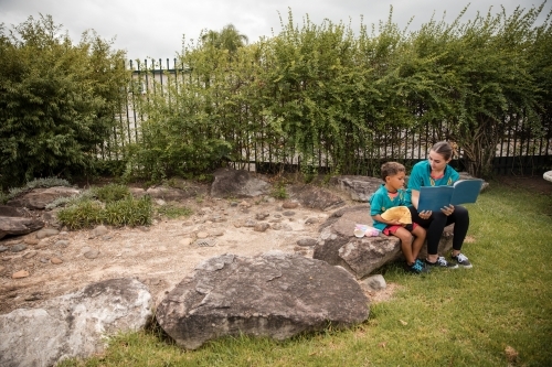 Carer reading with young boy outside - Australian Stock Image