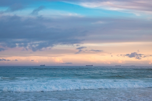 Cargo ships lined up at sea en route to Newcastle Harbour under a vibrant sunset sky - Australian Stock Image