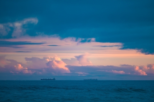 Cargo ships lined up at sea on their way to Newcastle Harbour under a vibrant sunset sky - Australian Stock Image