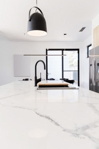 Carrara marble benchtop with black gooseneck kitchen tap and black pendant - Australian Stock Image