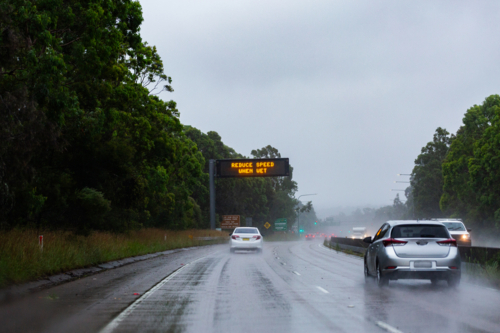 Cars traveling on slippery road with digital sign warning of hazardous driving conditions - Australian Stock Image