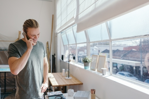 Casual guy on the phone smiling in a bright studio work space - Australian Stock Image