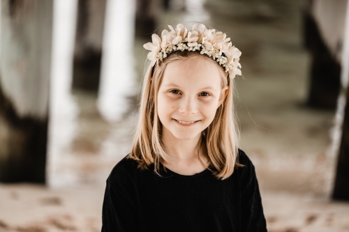 Caucasian girl standing underneath a pier at the beach wearing a flower head band - Australian Stock Image