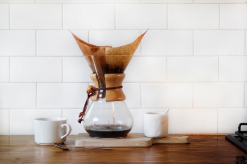 Chemex coffee filter on timber kitchen bench with coffee cup, sugar bowl against white subway tiles - Australian Stock Image