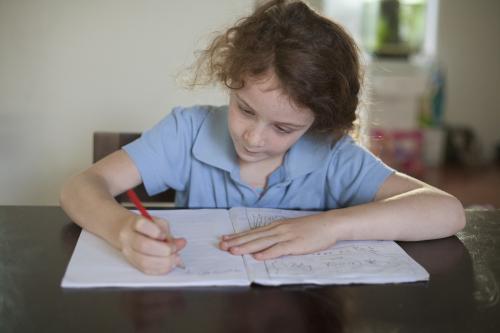 Child doing school homework at wooden desk. - Australian Stock Image